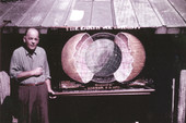 Unidentified man standing next to a Koreshan Unity poster showing "The Earth we inhabit".