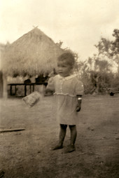 Portrait of a Seminole child near chickees at a village on the Tamiami Trail.