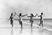 Four women in swimsuits running on Saint Petersburg beach.