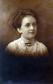 Close-up of a woman wearing a high-necked lace dress and glasses.