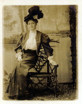 Woman with plumed hat sitting on edge of wooden chair