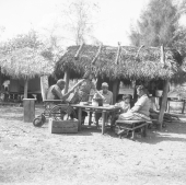 Seminole Indians sitting around a table, in front of chickee - Charlie Dixie Camp, Florida
