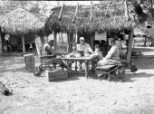 Seminole Indians sitting around a table in front of chickee - Charlie Dixie Camp, Florida