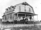 House with people on the porch and African American children in a cart
