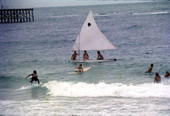 Sunfish sailboat and surfers sharing the waves at Miami Beach.