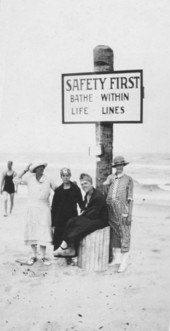 Unidentified women at the beach posing next to safety sign