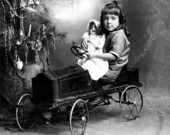 Unidentified girl holding her doll while sitting in a pedal car next to a Christmas tree - Pensacola, Florida.