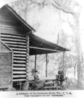 Married couple sitting on porch of log cabin by the Suwannee River.
