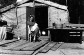 Young mother and child in front of their tarpaper house.