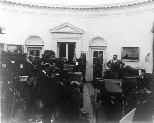 President John F. Kennedy in the Oval Office announcing the U.S. naval blockade of Cuba in front of a gathering of cameras and reporters.